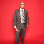 A man in a suit and tie standing against a red wall.