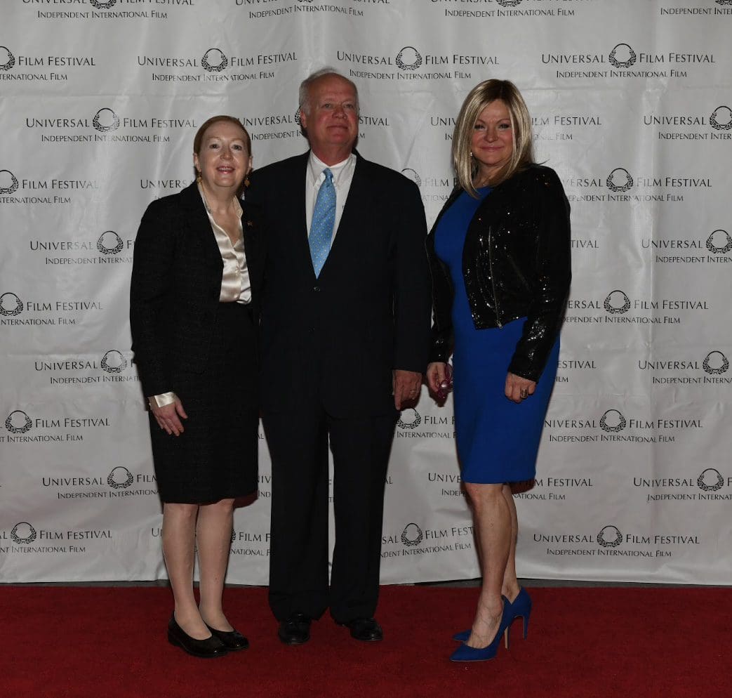 Three people posing for a picture in front of a white wall.