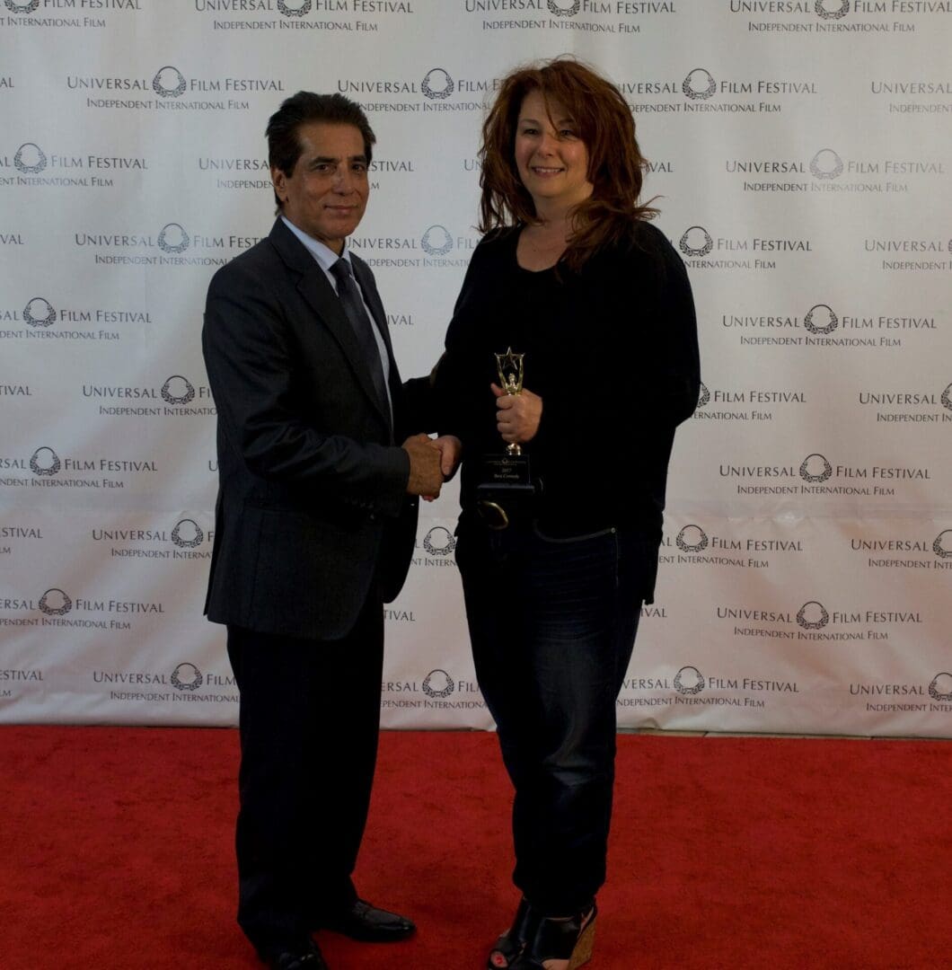 A man and woman shaking hands on the red carpet.