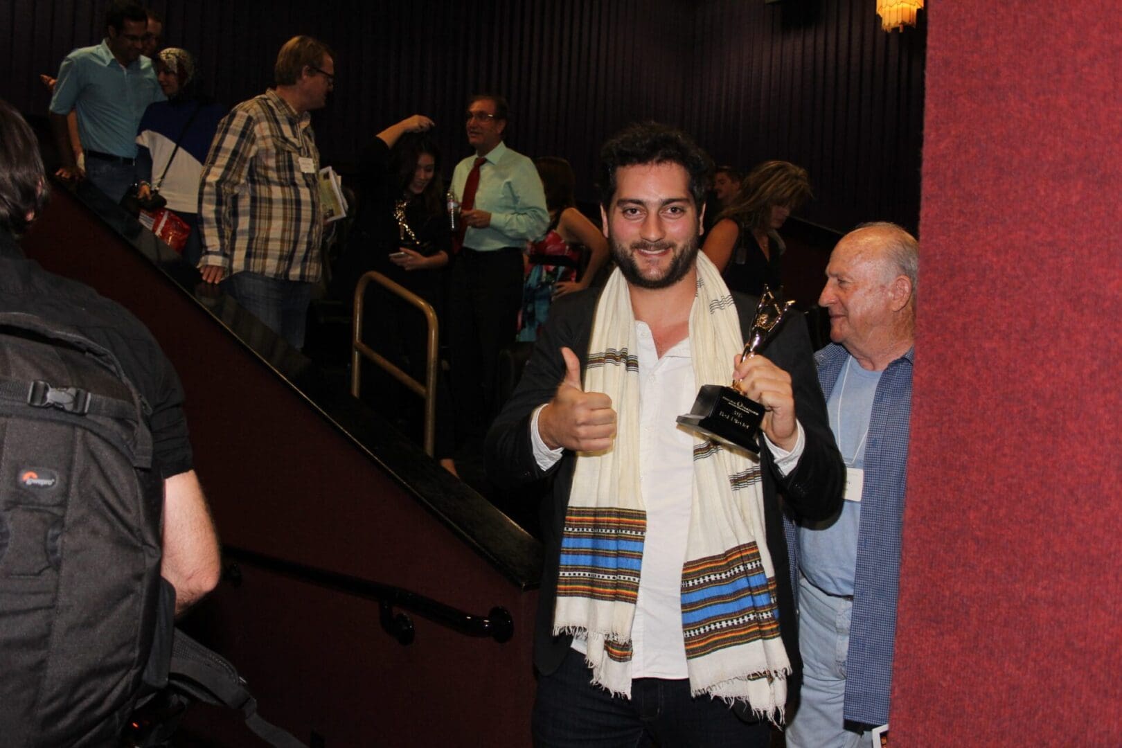 A man in a white and blue scarf is holding his thumbs up.