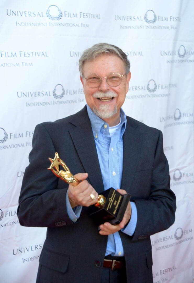 A man holding an award in front of a white wall.