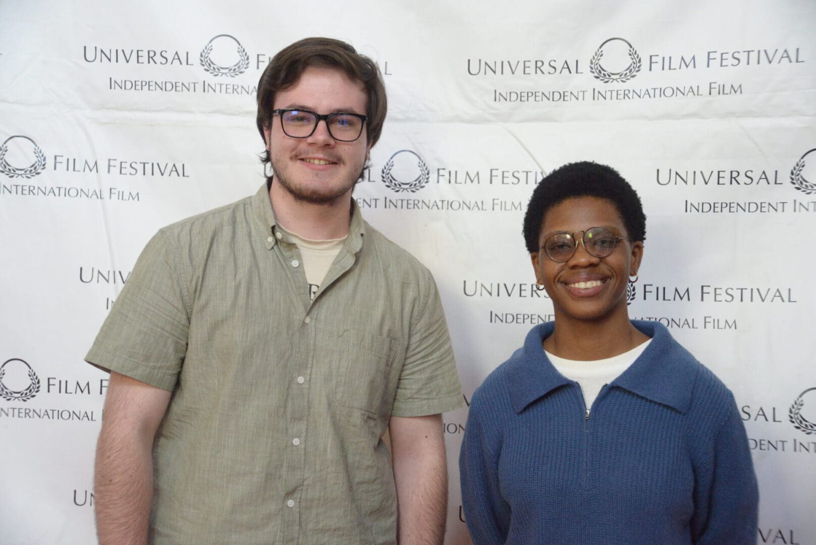 Two people standing in front of a white wall.